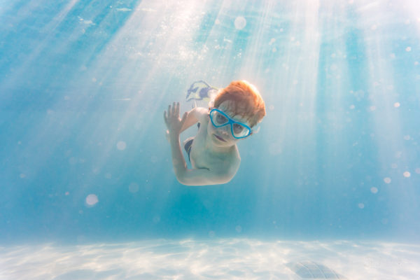Underwater view of redhaired boy diving in cool blue holiday swimming pool