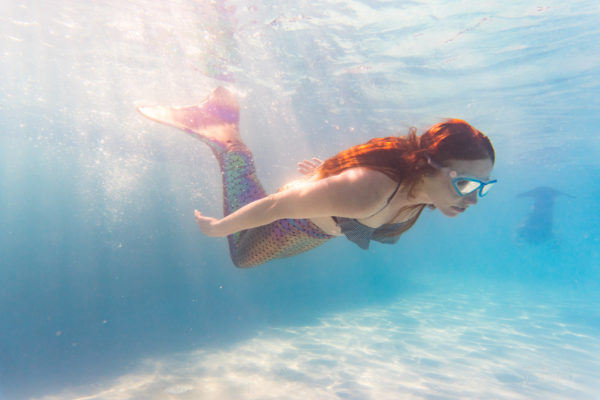 Underwater view of woman on holiday swimming in pool with colorful mermaid tail