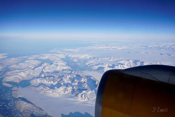 Traveler on vacation sees snow-covered mountains through airplane window